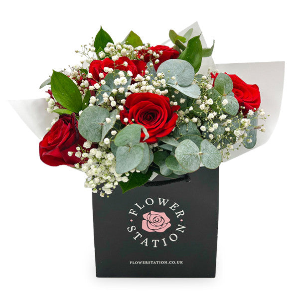 A bouquet of red roses and white baby's breath in a black bag